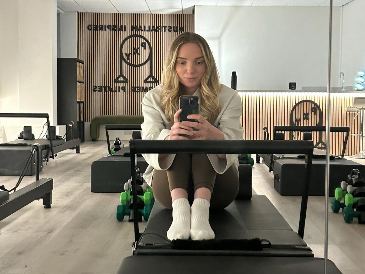 Olivia, founder of PXY Reformer Pilates, sitting on a reformer in the Didsbury studio
