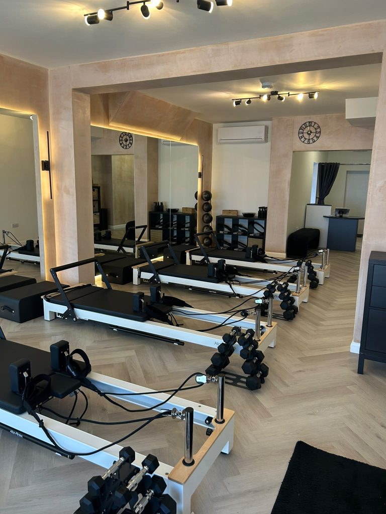 Rows of reformer beds and hand weights under warm lighting in the Chorlton studio